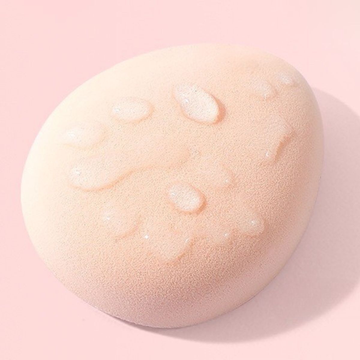 Une éponge de maquillage rose pâle avec des gouttes d'eau sur la surface.