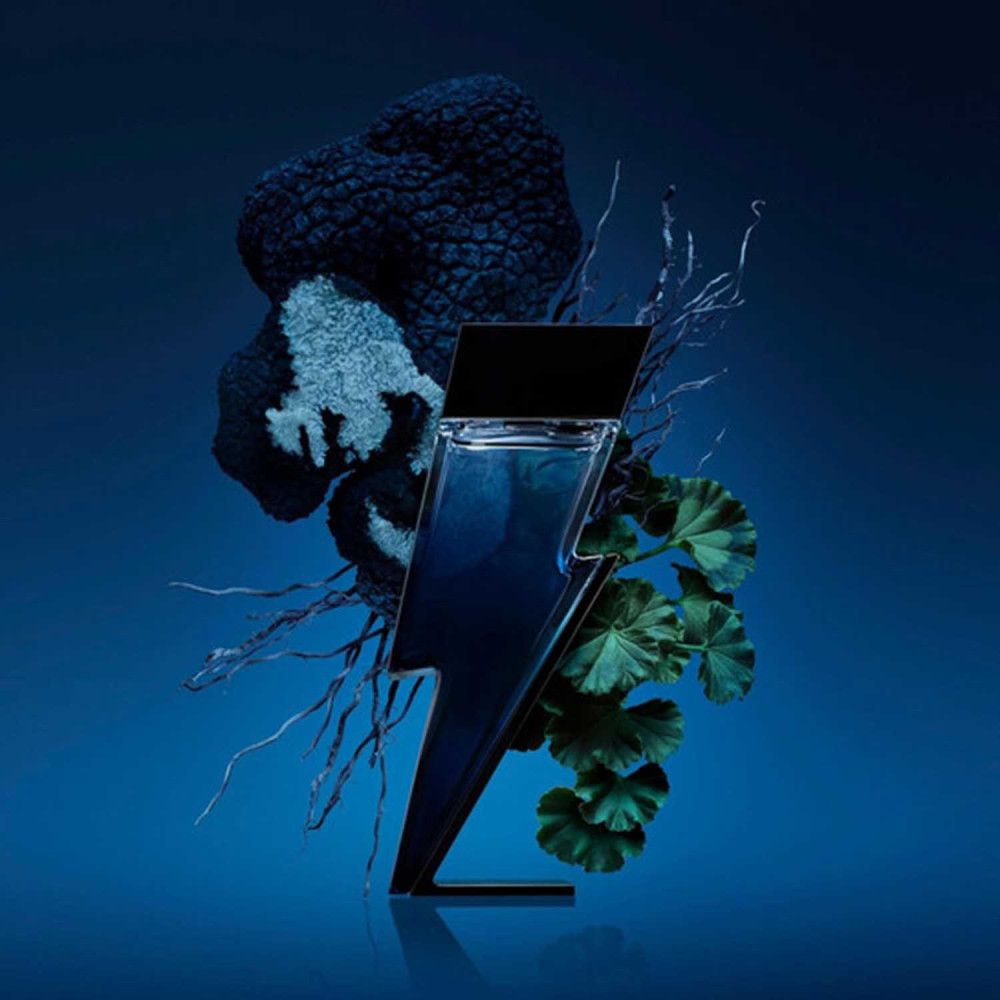 Flacon noir en forme d'éclair, entouré de plantes et de branches. Liquide bleu visible.