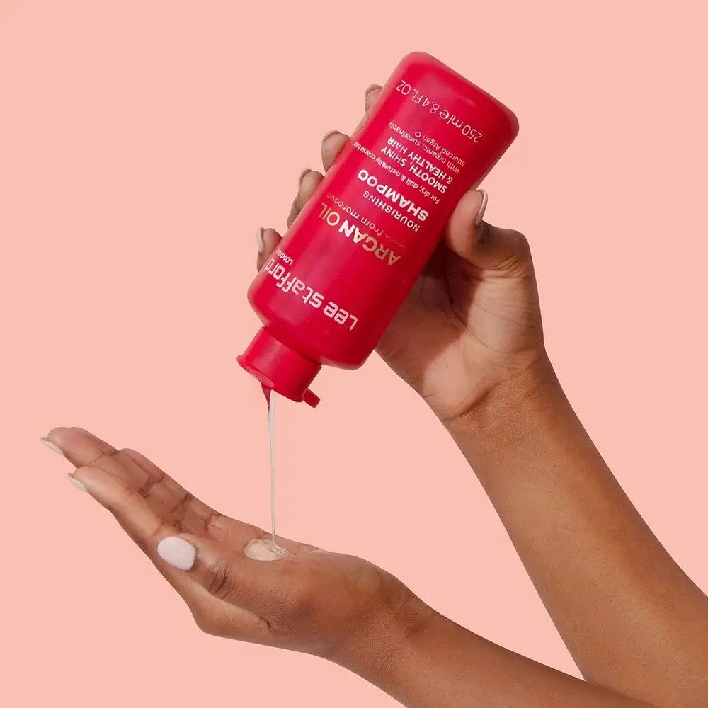 Rode shampoo fles wordt in de hand gegoten. Opschrift: Argan Oil, Shampoo. Handen houden de fles vast en vangen het product op.
