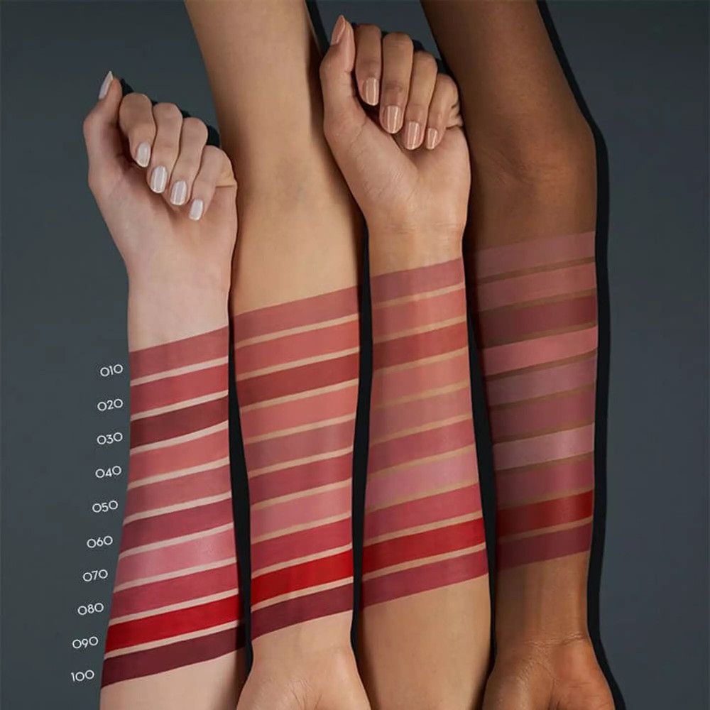 Bras avec des échantillons de rouge à lèvres dans différentes nuances de rouge. Différents tons de peau. Texte: 010 à 100.