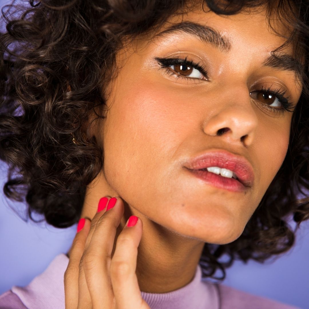 Close-up van een vrouw met make-up. Ze raakt haar nek aan. Lippenstift en nagellak zichtbaar.