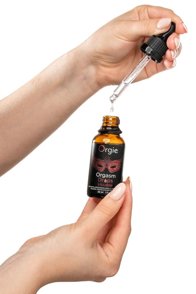 Mains tenant un flacon Orgie Orgasm Drops Kissable. Pipette laissant tomber du liquide.