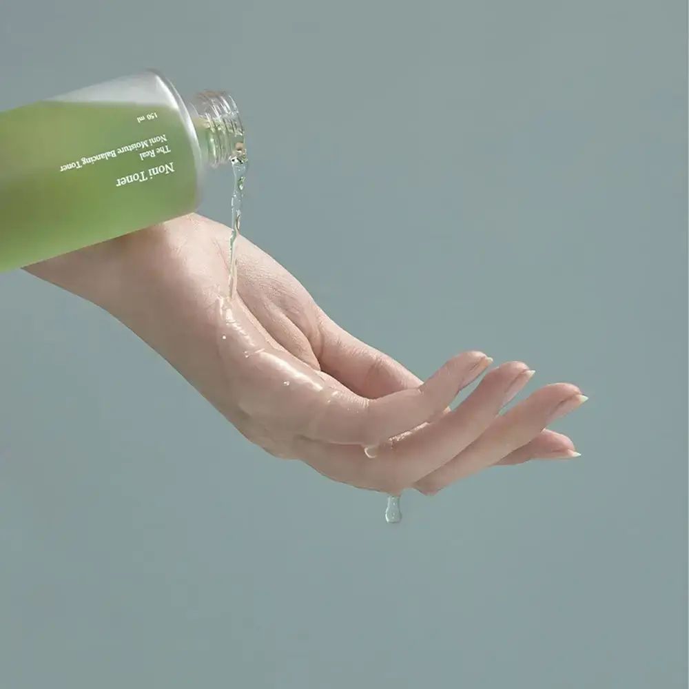 Vloeistof uit een fles op een hand gegoten. De vloeistof is helder en druppelt op de huid.