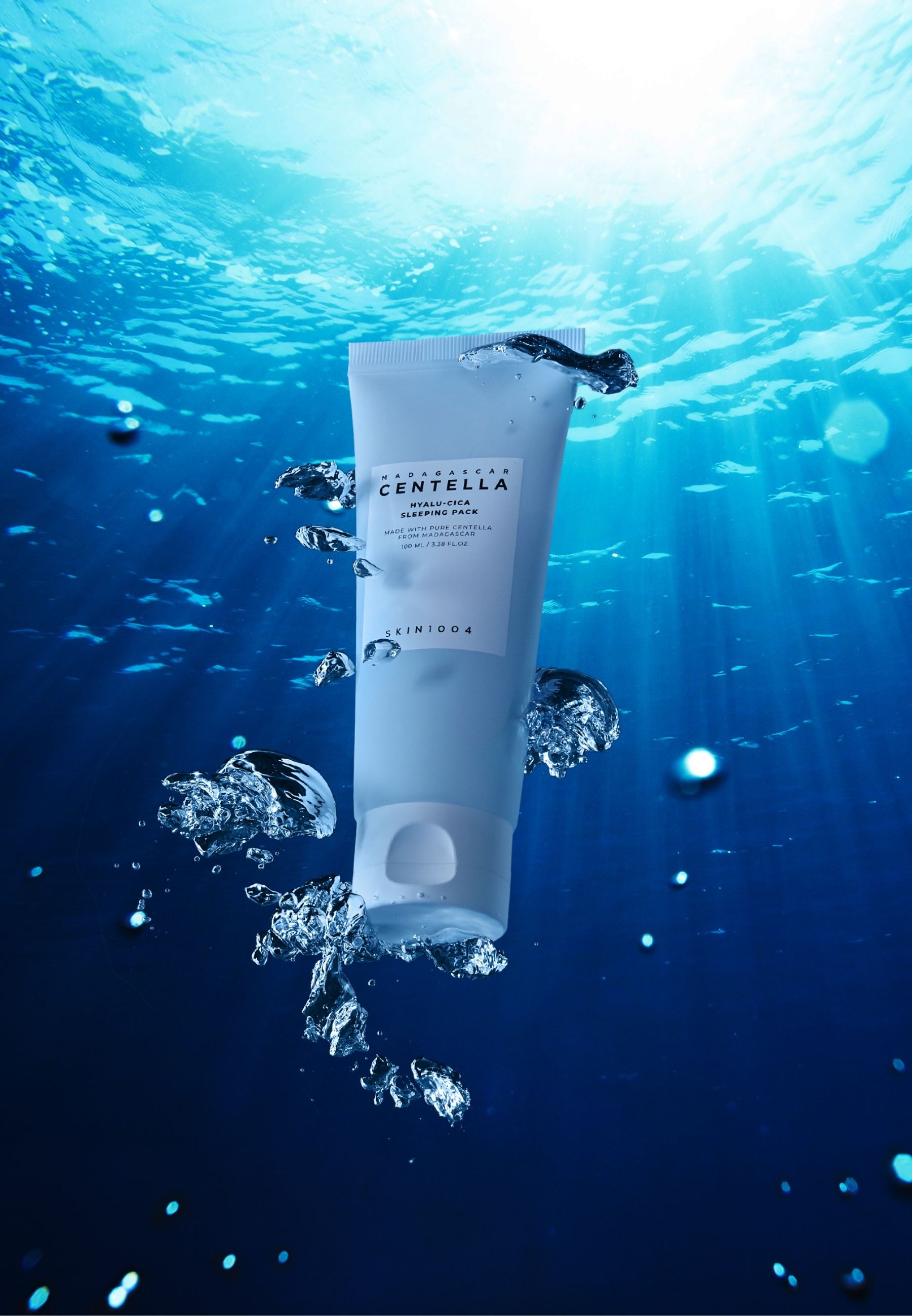 Lichtblauwe tube onder water. Opschrift: MADAGASCAR CENTELLA, HYALU-CICA SLEEPING PACK, SKIN1004. Waterbellen.