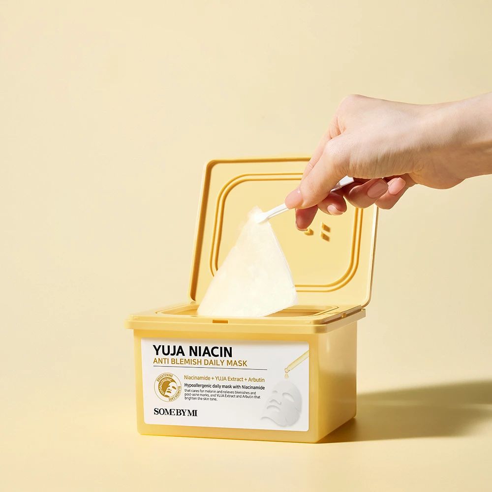 Open gele maskerdoos. Een hand neemt een masker eruit. Opschrift: Yuja Niacin Anti-Blemish Daily Mask.