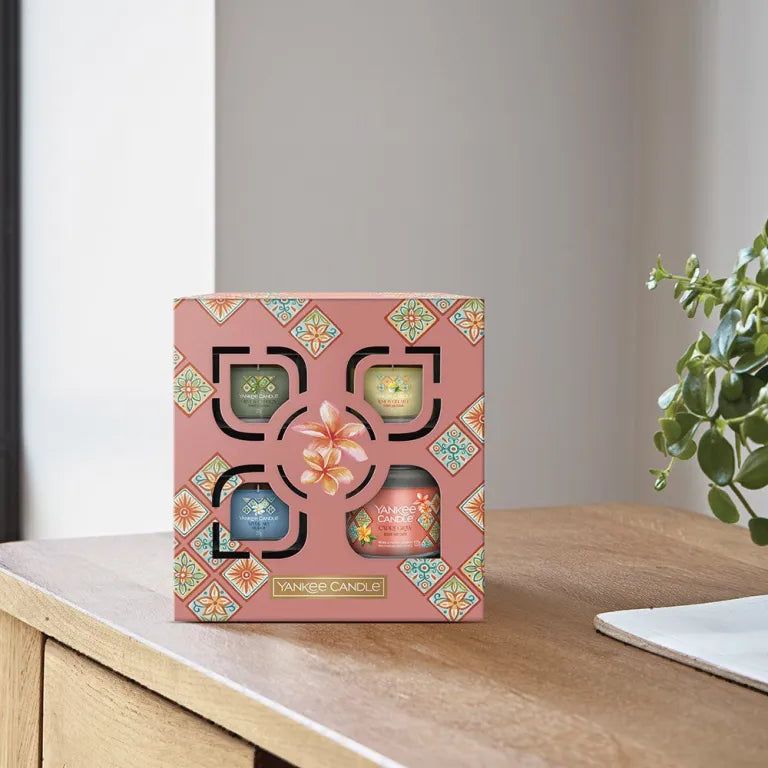 Coffret cadeau Yankee Candle avec quatre bougies votives. Boîte rose sur table en bois. Logo visible.
