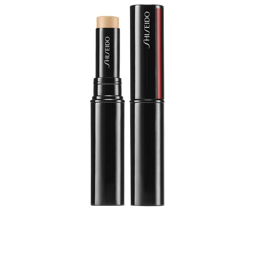 Correcteur de teint en bâton noir avec produit beige. Capuchon à côté. Logo Shiseido sur le bâton et le capuchon. Bande rouge sur le capuchon.