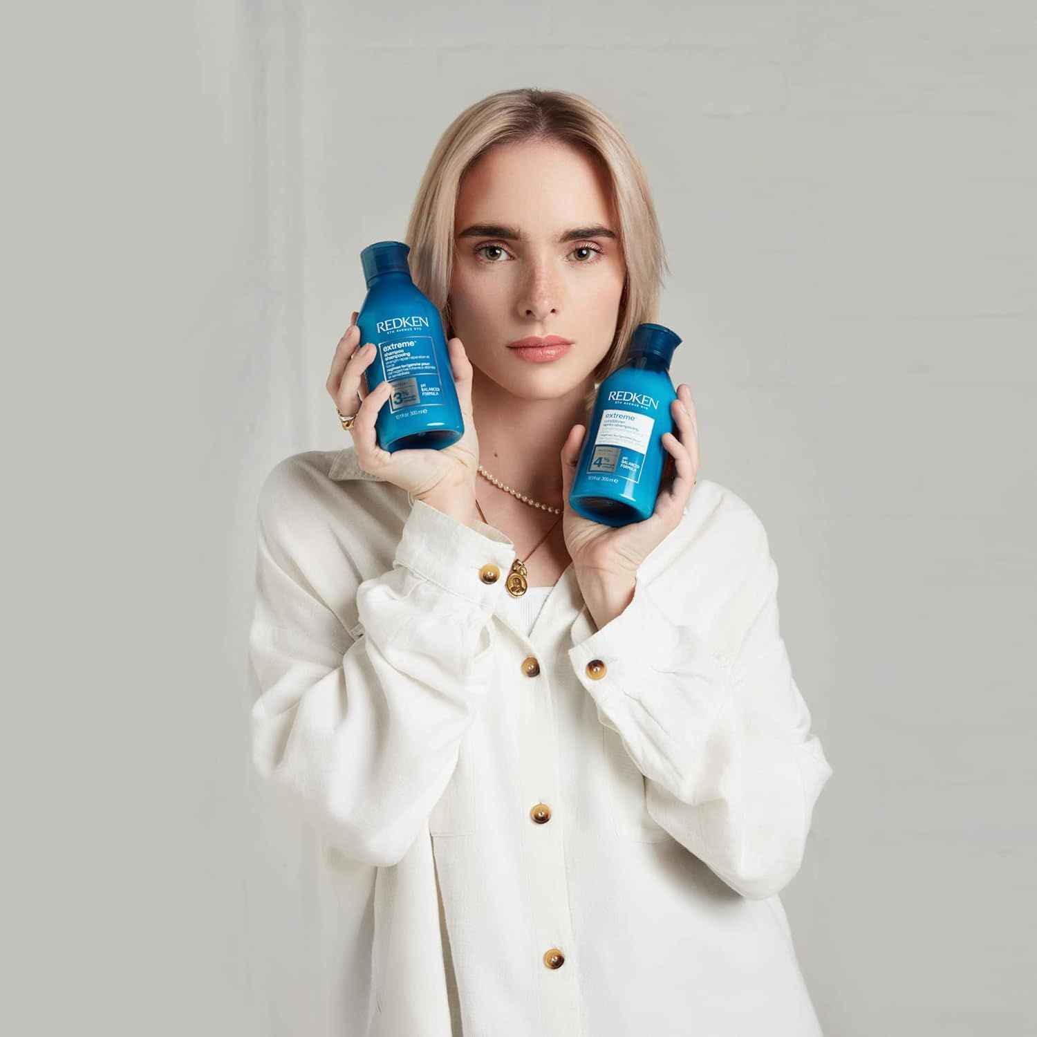 Een vrouw houdt twee blauwe flessen vast. Beide flessen hebben productnamen en logo's.