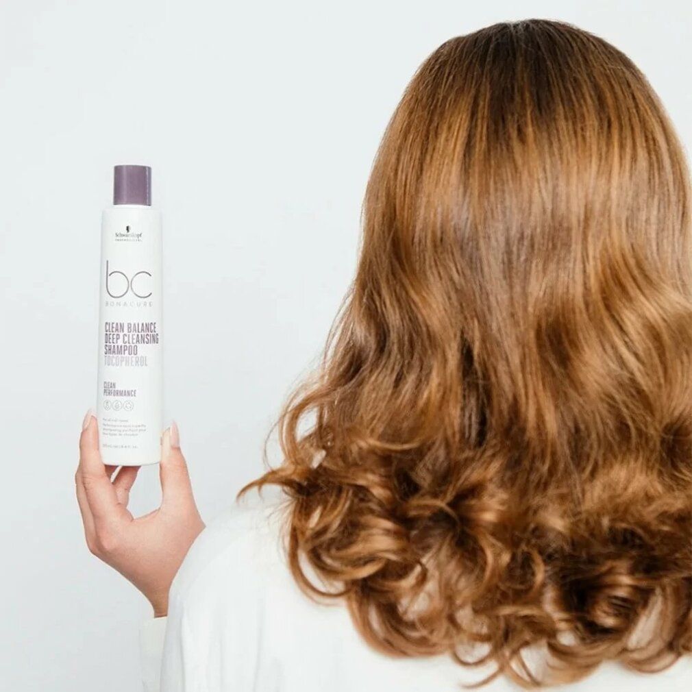 Persoon houdt shampoo fles vast. Opschrift: BC Bonacure Clean Balance Deep Cleansing Shampoo. Lang, golvend haar.