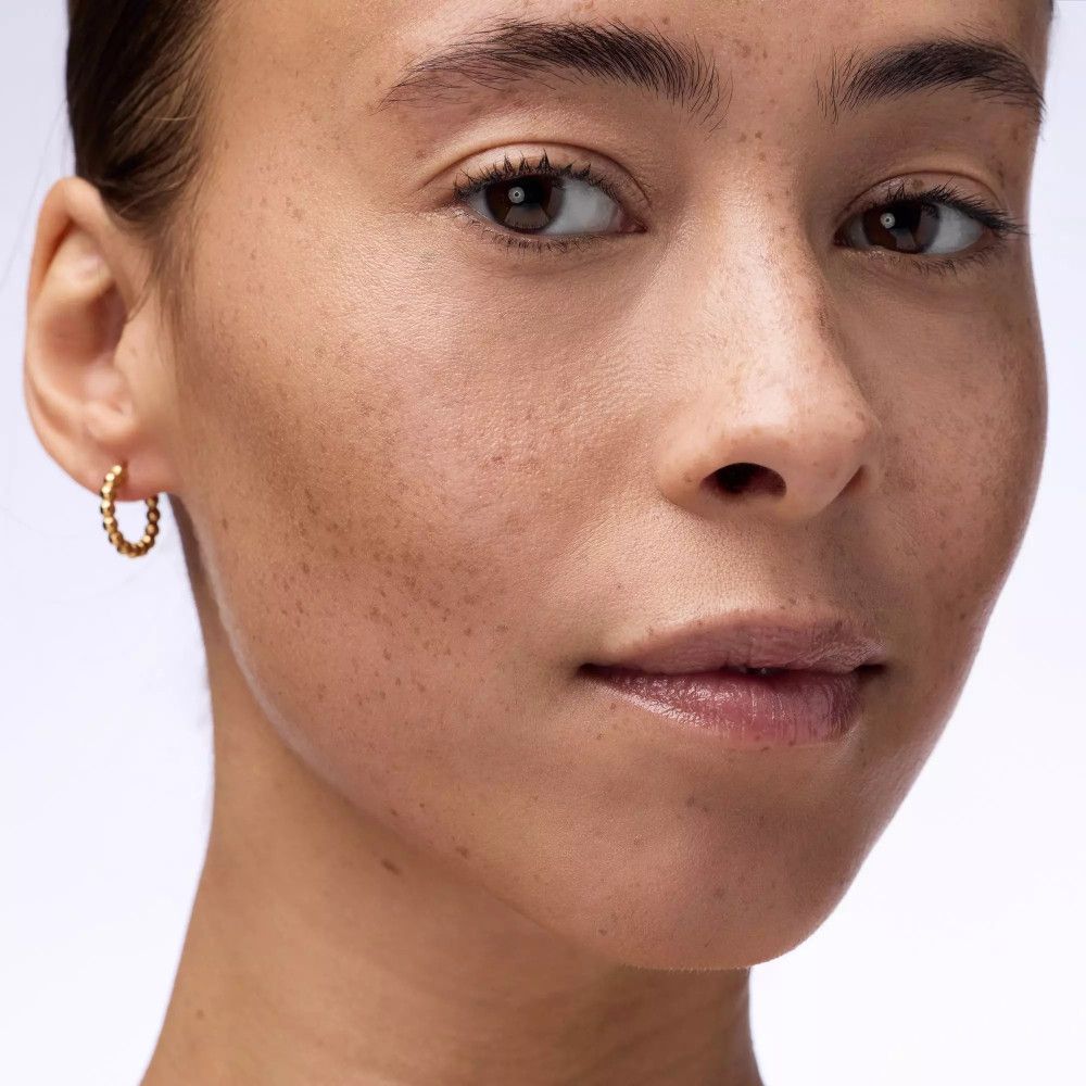 Close-up van een gezicht. Vrouw met sproeten, gouden oorbel. Bruine ogen, lichte teint.