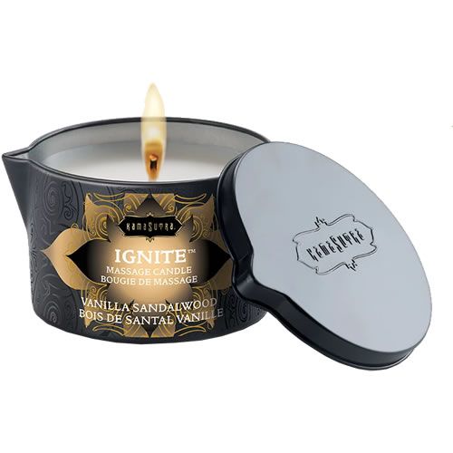 Bougie de massage avec couvercle. Boîte noire avec motif doré et texte. Flamme allumée. Couvercle à côté.