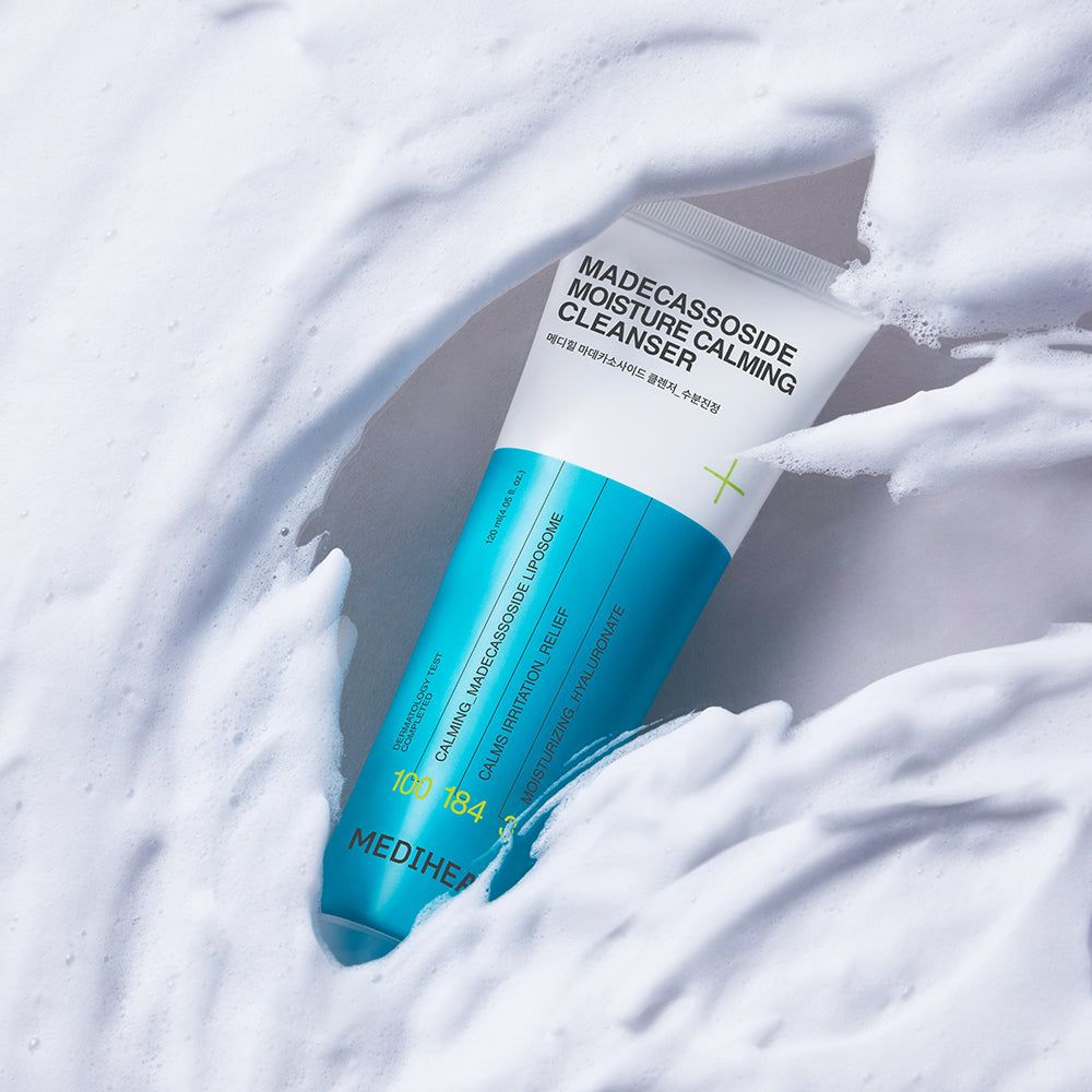 Tube blanc et bleu dans de la mousse. Inscription: Madecassoside Moisture Calming Cleanser. Marque: MEDIHEAL. Texte en anglais et coréen.