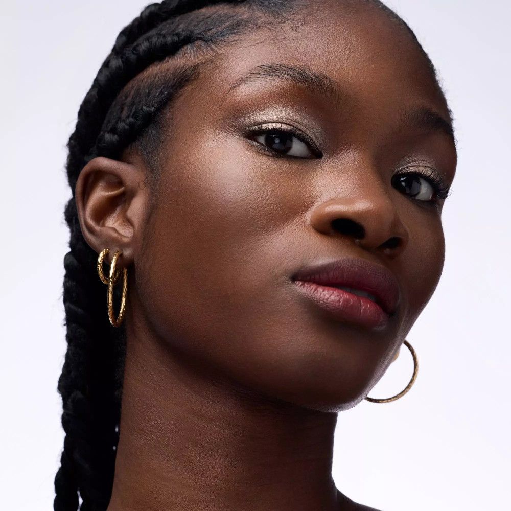 Portrait d'une femme avec fard à paupières métallique. Elle porte des créoles dorées. Peau foncée.