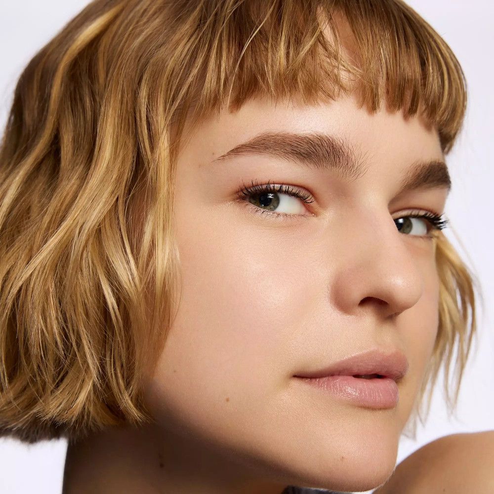 Portrait d'une femme aux cheveux blonds et frange. Sourcils naturels, regard ouvert, lèvres légèrement maquillées.