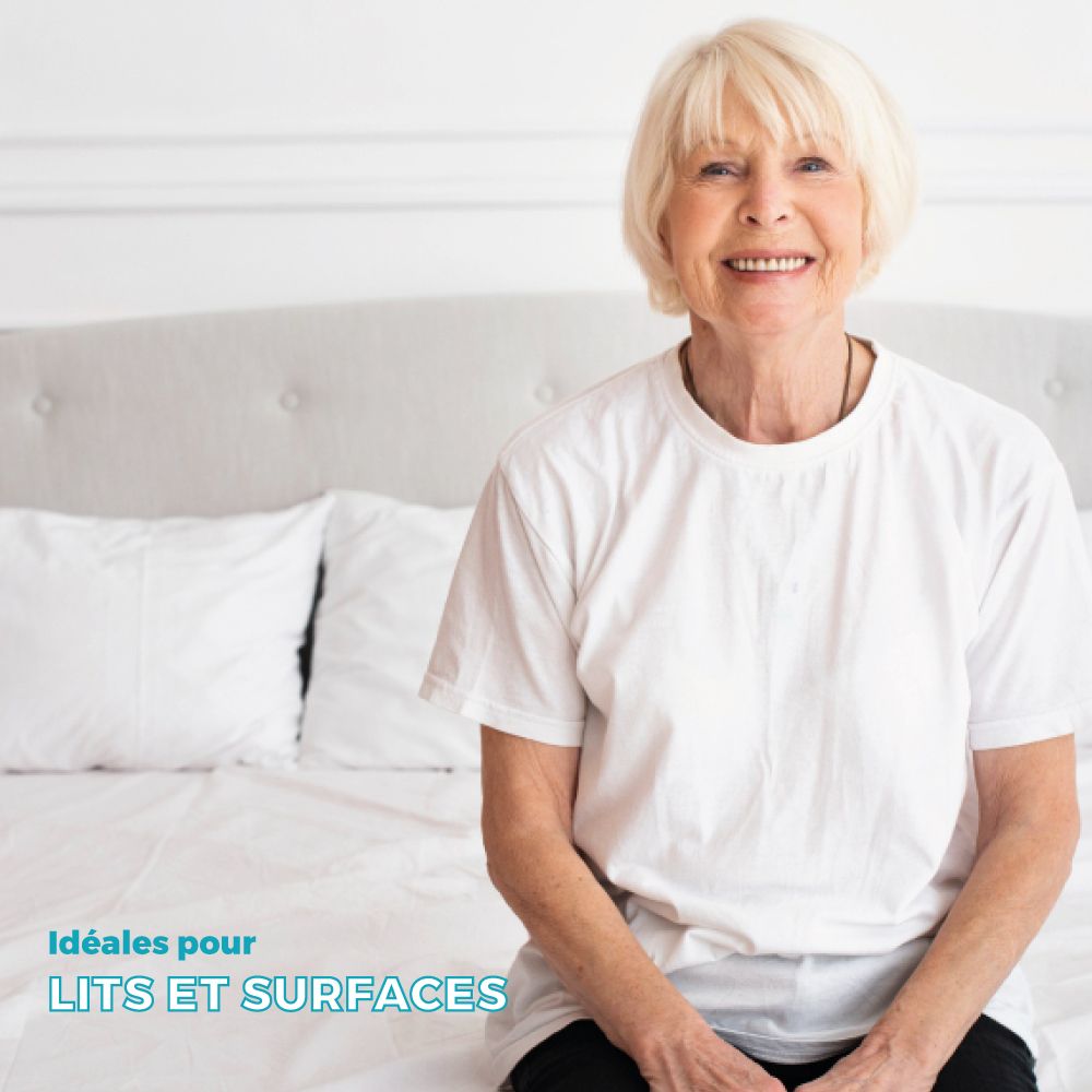 Femme âgée assise sur un lit. Oreillers blancs sur le lit. Inscription : Idéales pour lits et surfaces.