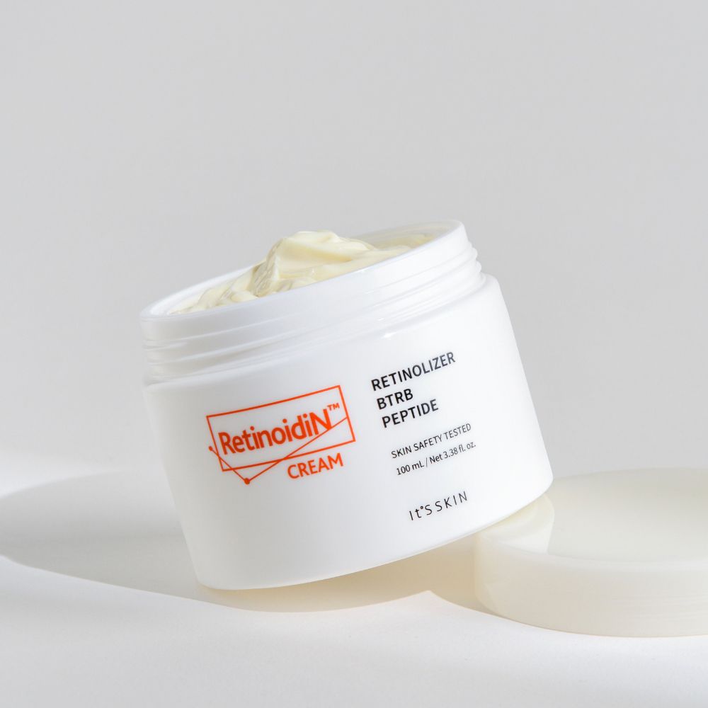 Pot blanc avec logo orange et texte Retinoidin Cream. Couvercle à côté. Crème visible.