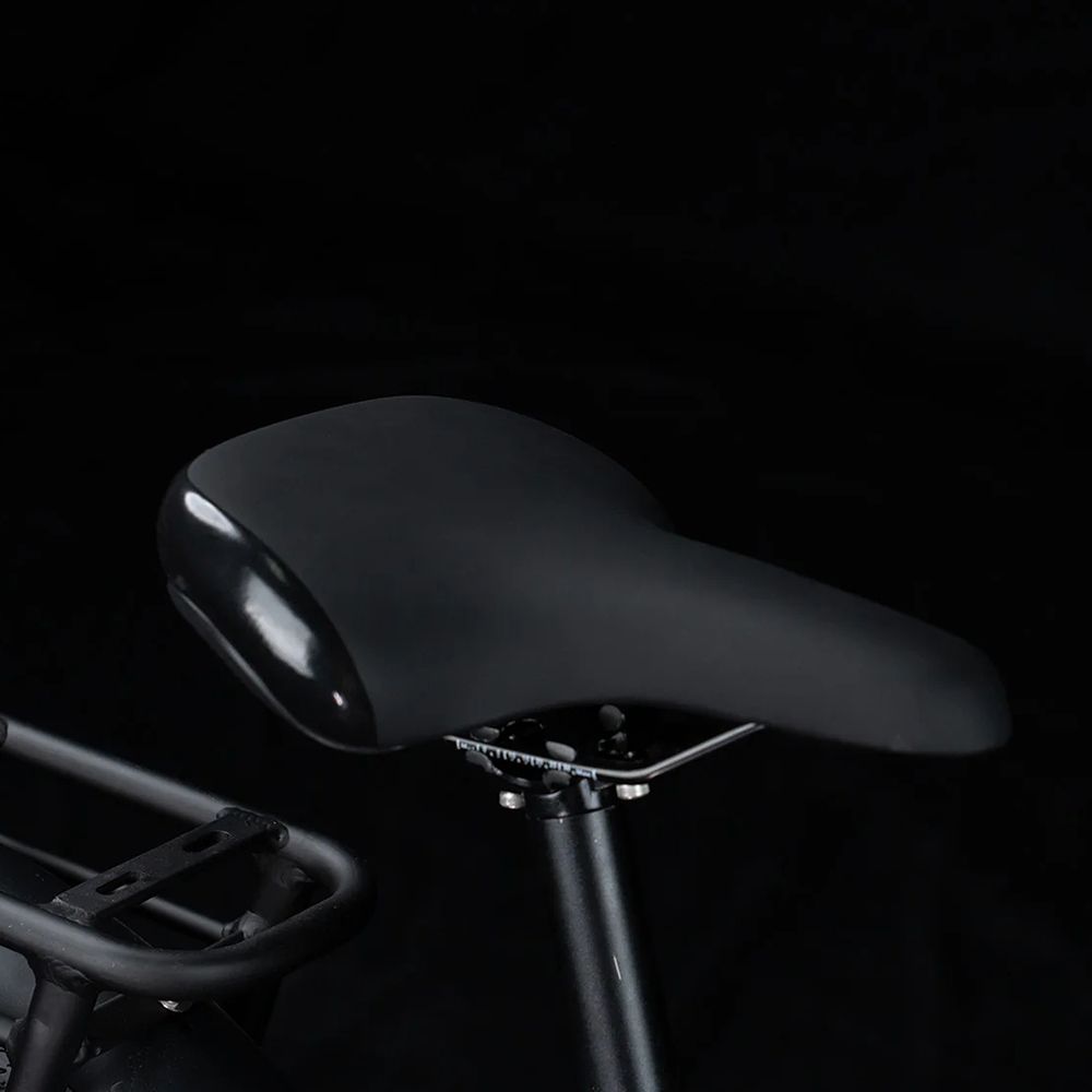 Selle de vélo noire, brillante. Sur fond noir. Fait partie d'un vélo électrique.