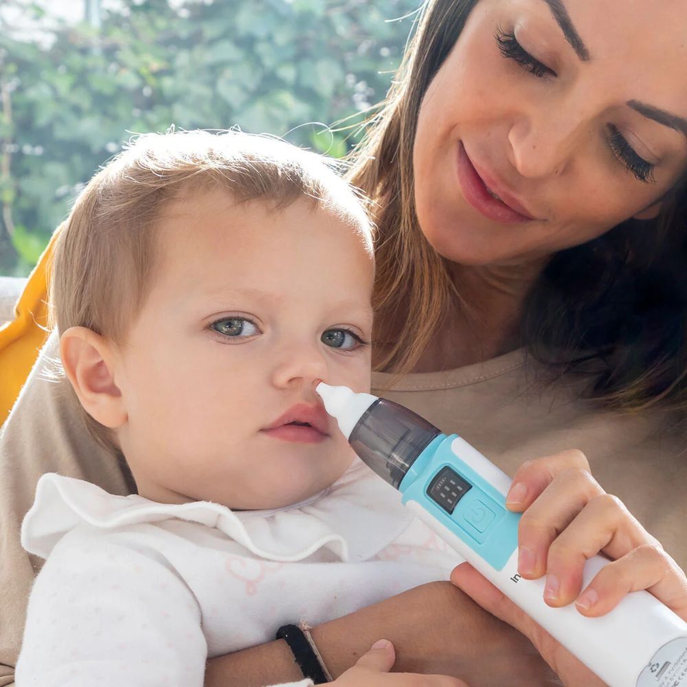 Een baby krijgt een neuszuiging. Het apparaat is wit en blauw. Een moeder houdt de baby vast.