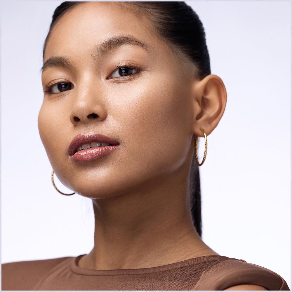 Portrait d'une femme avec un repulpeur de lèvres. Elle porte des créoles dorées et a un rouge à lèvres brillant.