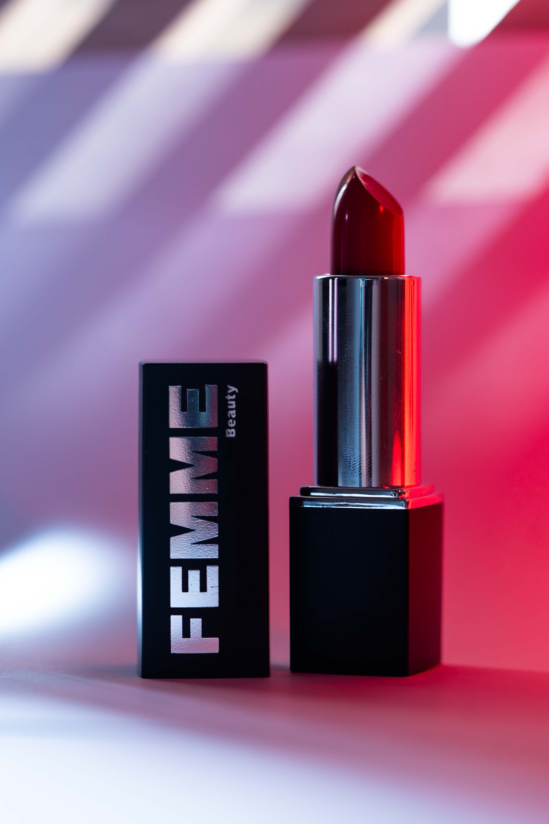 FEMME Visionary Satin Lipstick in rood, dop eraf, verlicht met rood en paars licht.