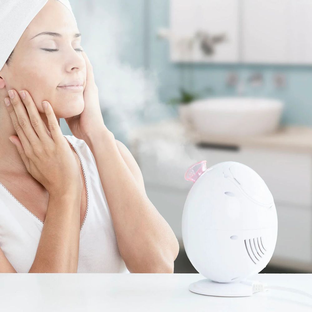 Appareil ovale blanc avec accents roses. Une personne avec une serviette sur le visage. De la vapeur s'élève.