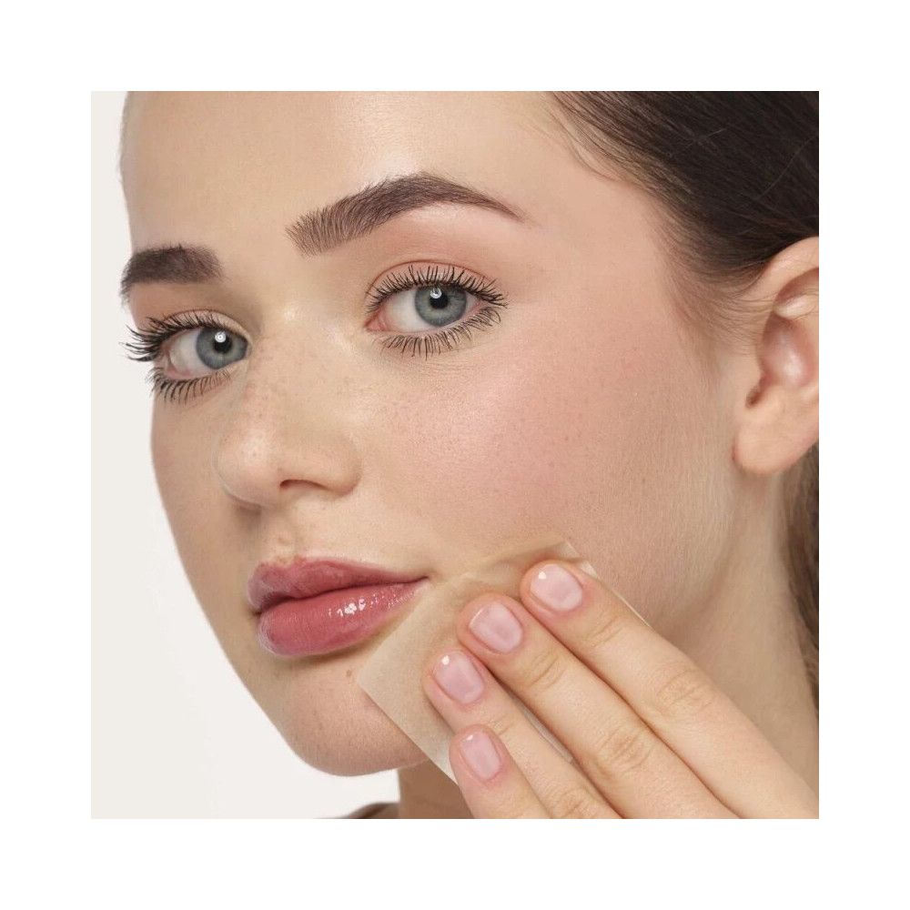 Vrouw met lichte huid gebruikt vierkant olie-absorberend papier op haar huid. Papier raakt wang.