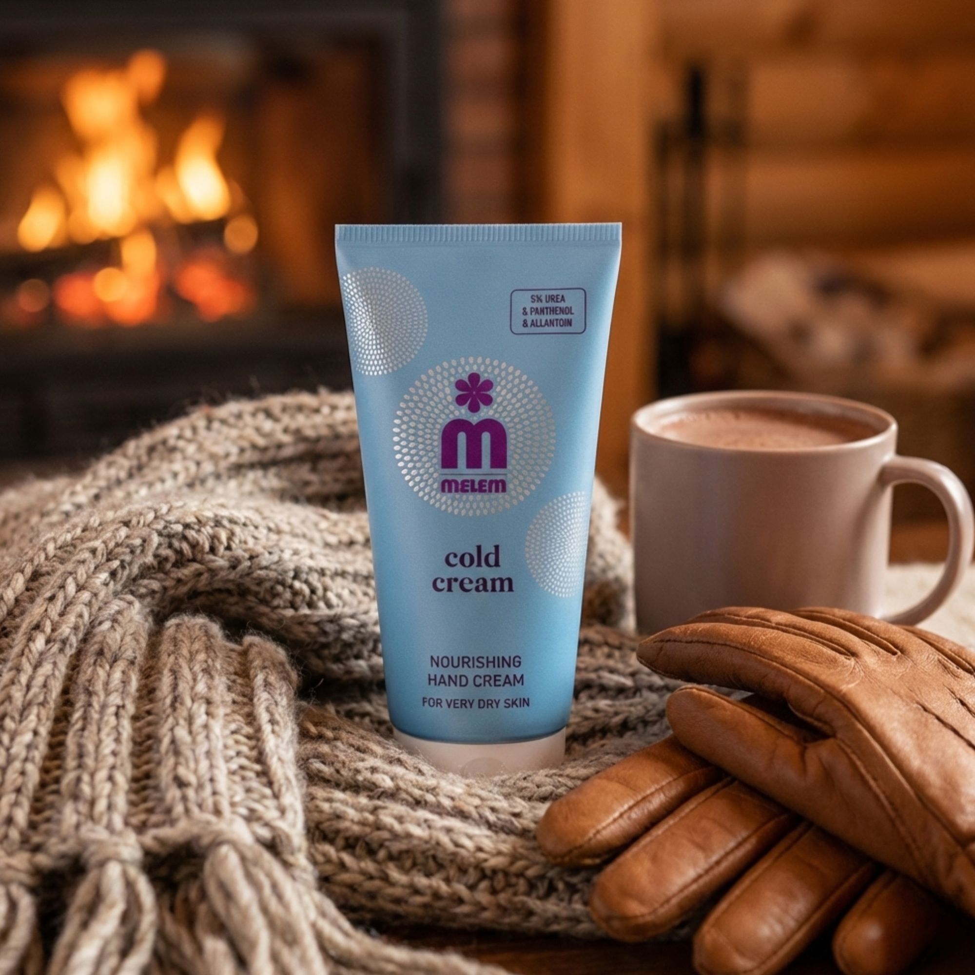 Tube bleu clair "Melem Cold Cream" sur écharpe en laine. Tasse et gants en cuir à côté. Cheminée en arrière-plan.