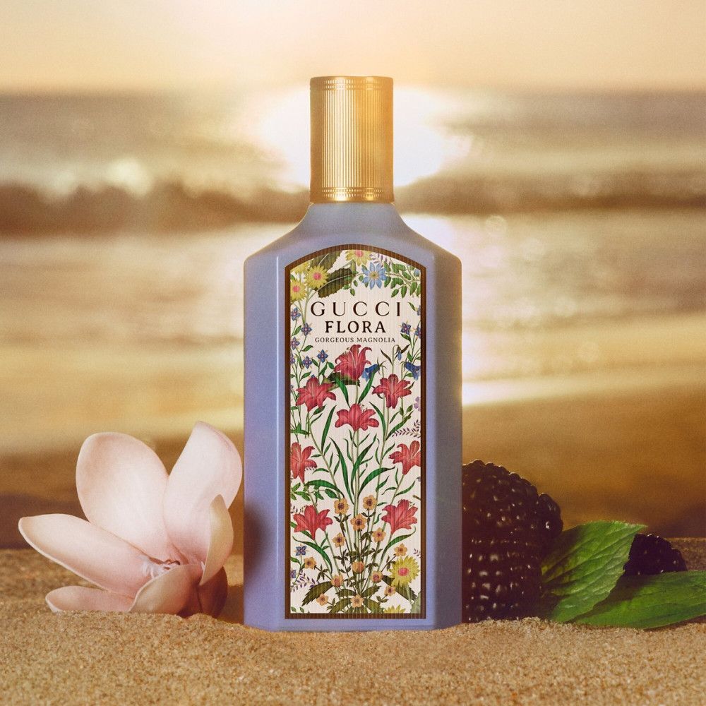 Flacon avec étiquette florale. Bouchon doré. Inscription : Gucci Flora Gorgeous Magnolia. Fond de plage.