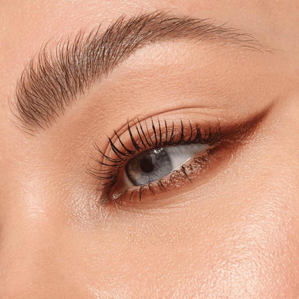 Gros plan sur un œil avec un trait de khôl marron. Les cils sont maquillés.