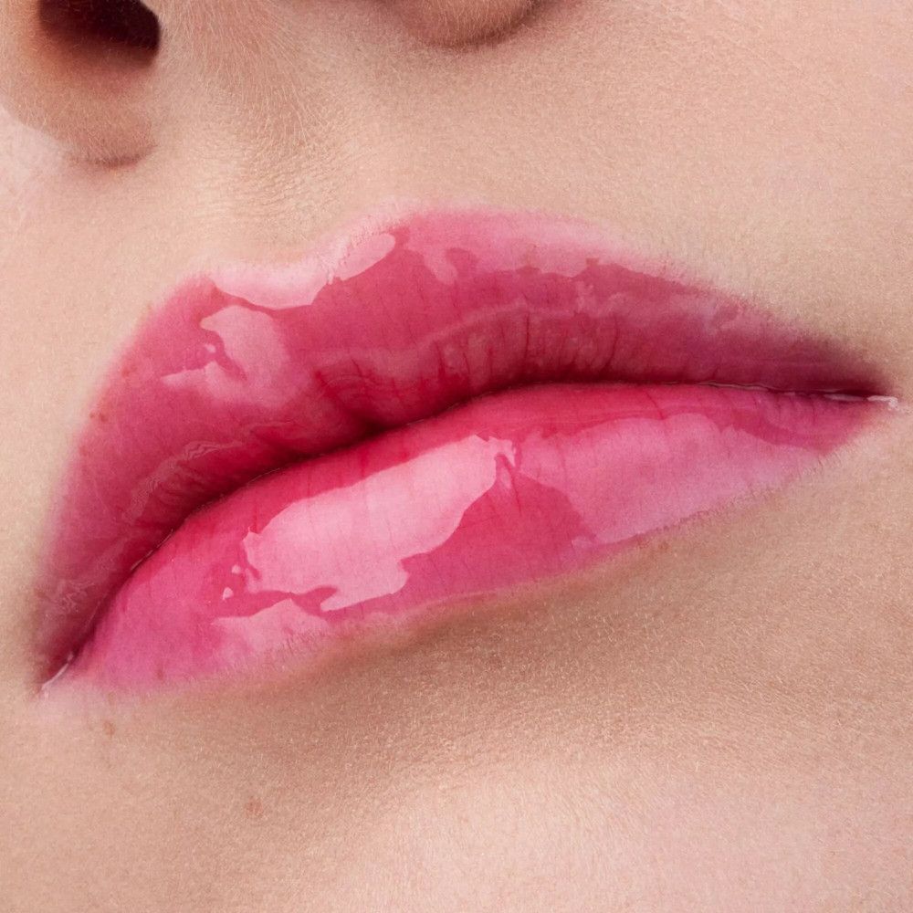 Close-up van lippen met glanzende, roze lipolie. Open lippen, tanden zichtbaar.
