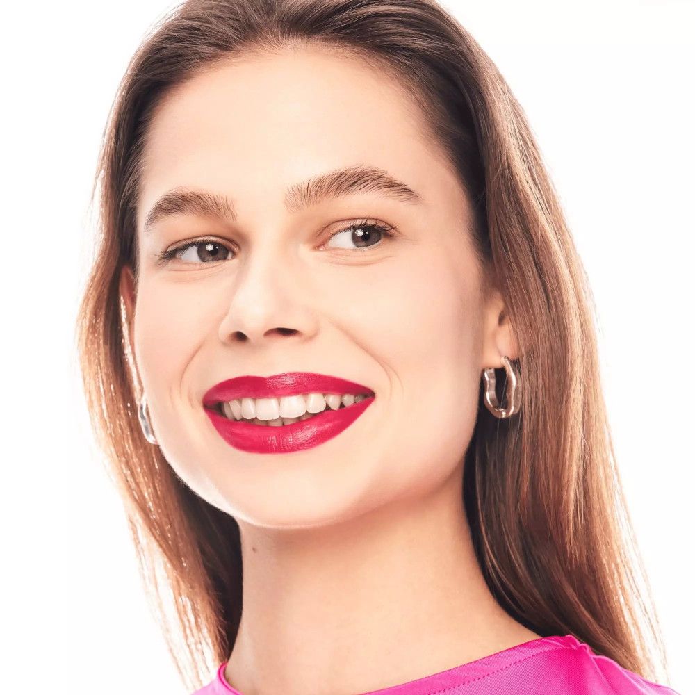 Vrouw met lippenstift. Ze draagt een roze top en zilveren oorbellen. Haar mond is opgemaakt met rode lippenstift.