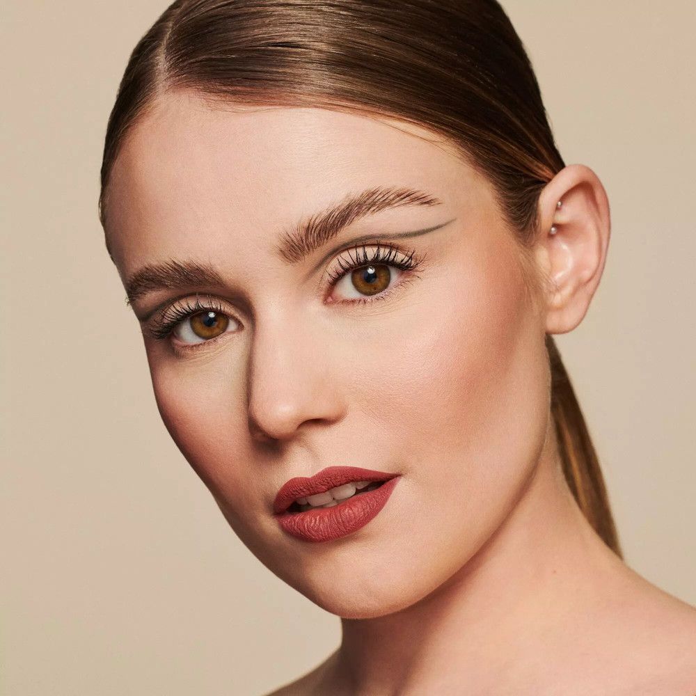 Portrait d'une femme maquillée. Accent sur les yeux et les lèvres. Mascara, eye-liner et rouge à lèvres. Fond beige.