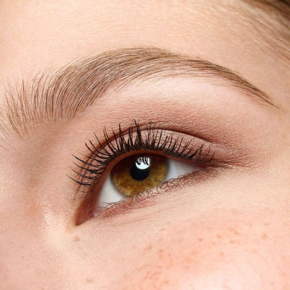 Gros plan sur un œil avec de l'ombre à paupières crème. Yeux bruns, longs cils.