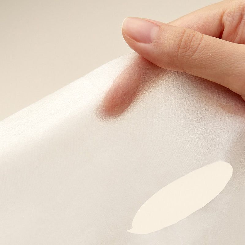 Gros plan d'une main tenant une feuille blanche translucide. Une tache crème est visible.