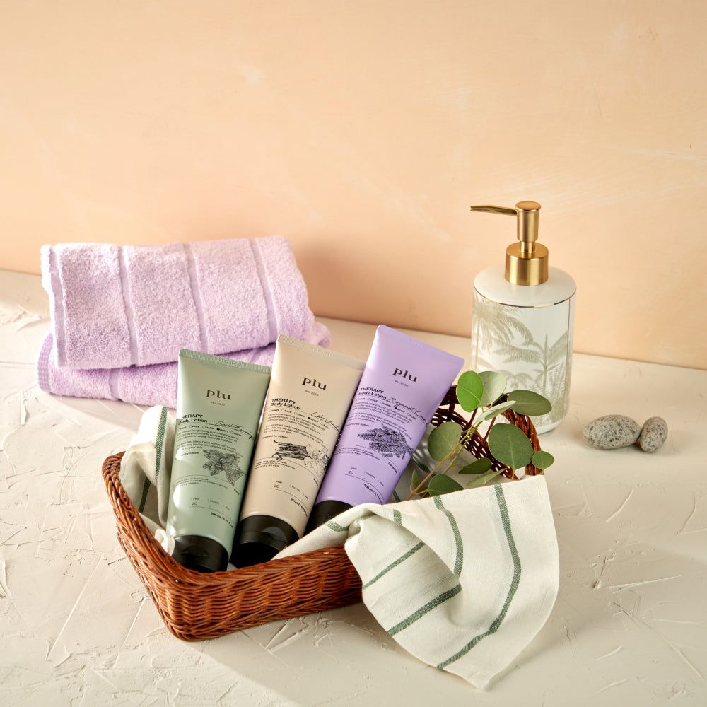 Panier avec trois tubes 'plu AROMA Body Lotion' de couleurs différentes, serviettes et distributeur de savon.