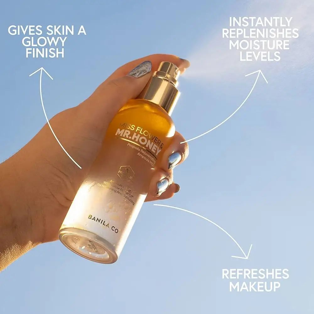 Hand houdt gezichtsspray vast. Gouden dop, gelige vloeistof. Opschrift: Miss Flower & Mr. Honey. Spuitnevel zichtbaar.