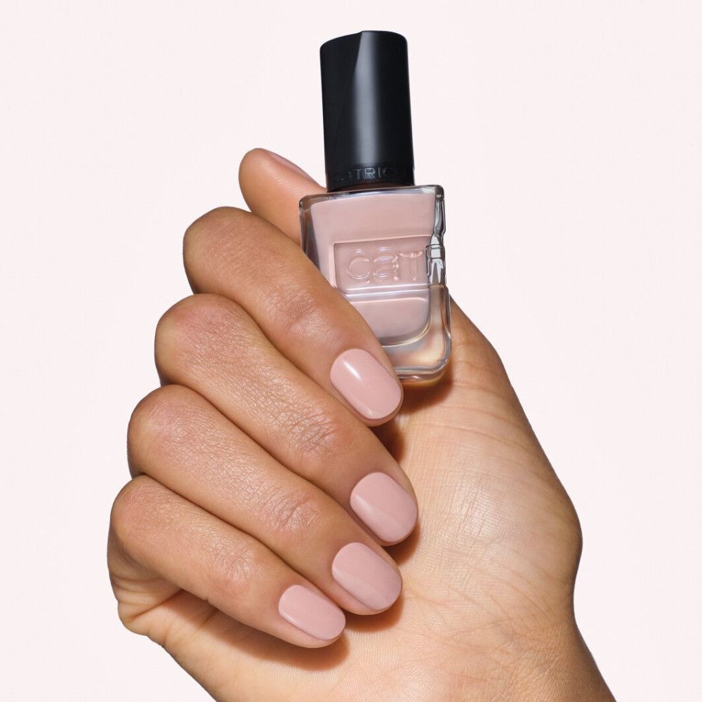 Een hand houdt een fles lichtroze nagellak met zwarte dop vast. De nagels zijn bijpassend gelakt.