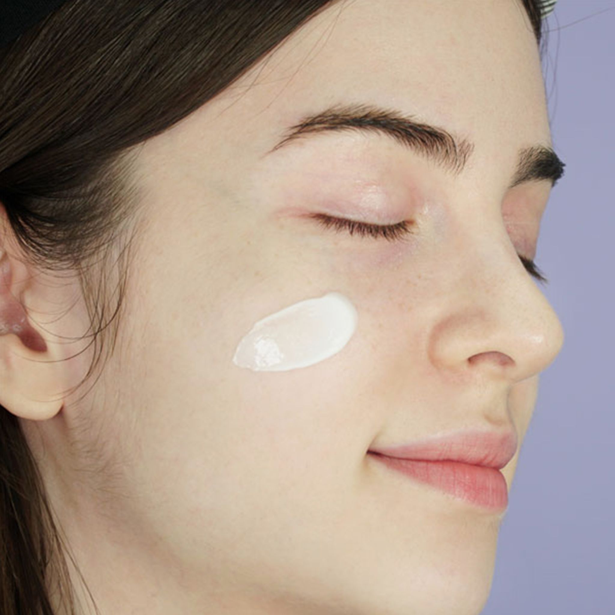 Close-up van een gezicht met crème op de wang. Persoon met gesloten ogen. Lichte crème.