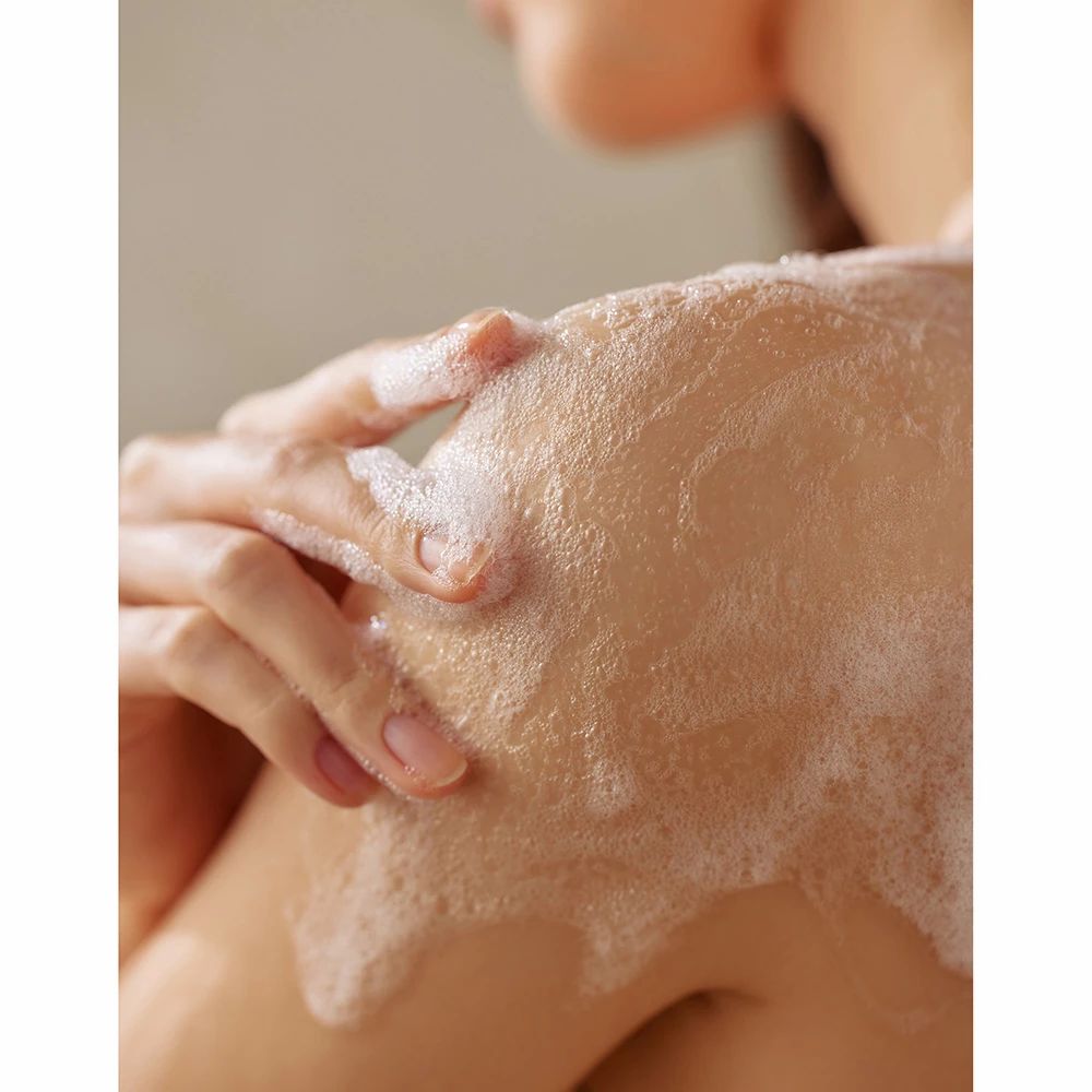 Épaule recouverte de mousse blanche. Mains frottant la mousse sur la peau.