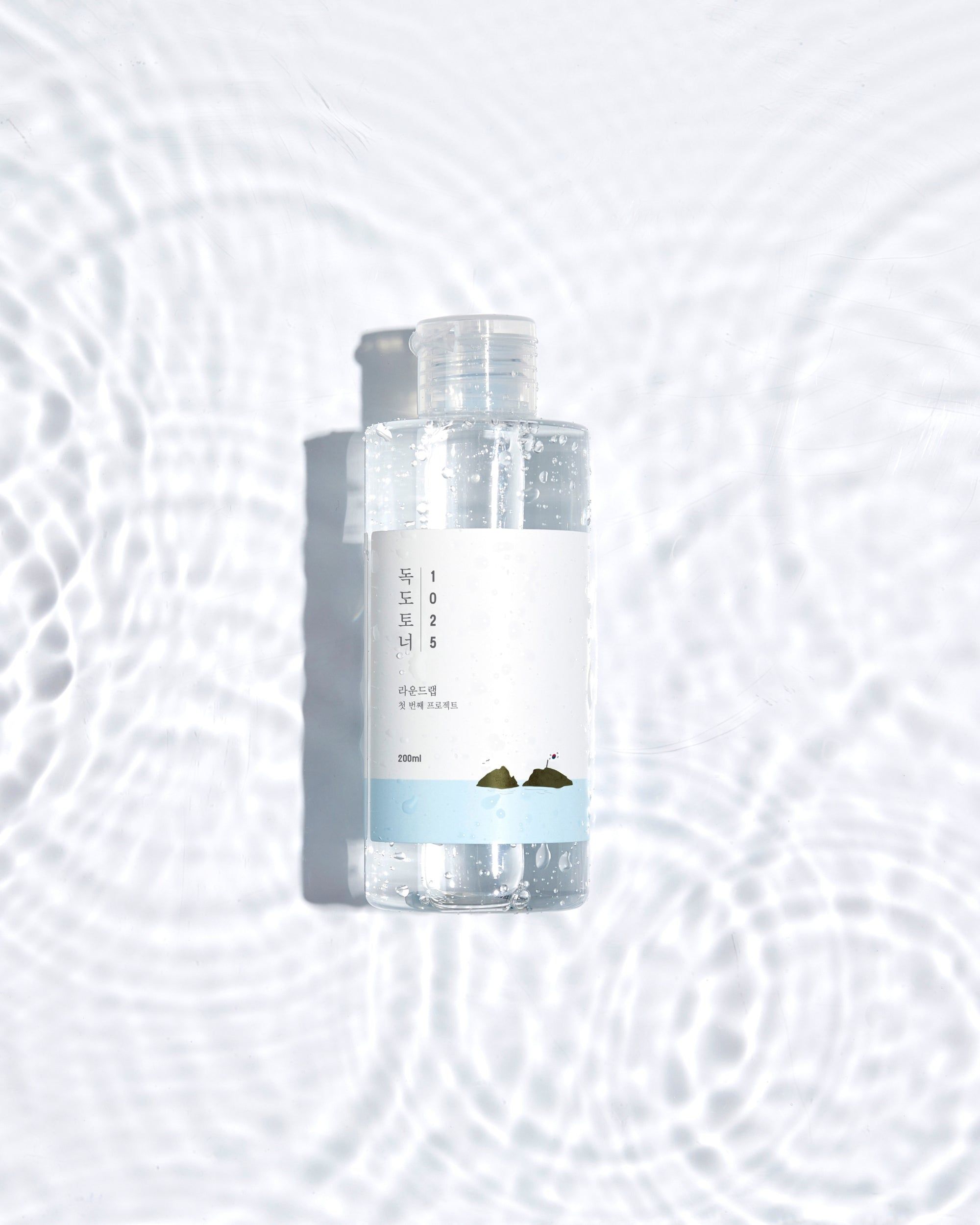 Flacon transparent avec étiquette blanche. Flacon dans l'eau. Motif de vagues. Fond blanc clair.