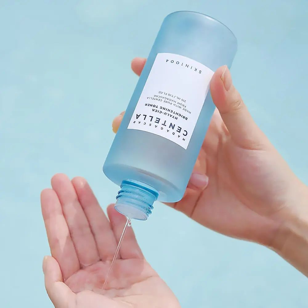 Blauw-transparante fles, vloeistof wordt in de hand gegoten. Opschrift: SKIN1004, MADAGASCAR CENTELLA, HYALU-CICA.