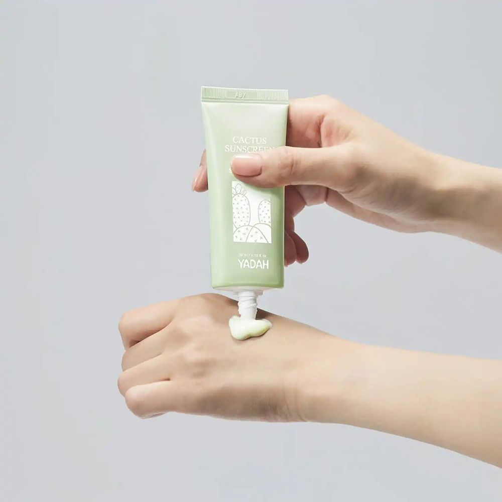 Handen houden groene tube "Cactus Sunscreen" en persen crème uit. Merk "YADAH".