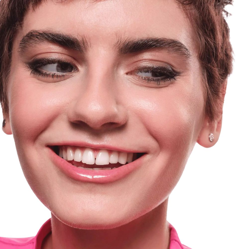 Gros plan d'une femme souriante avec de l'eyeliner sur les paupières. Elle porte un pull rose.