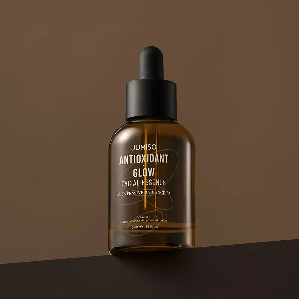 Bruine glazen fles met zwarte dop en pipet. Opschrift: JUMISO ANTIOXIDANT GLOW FACIAL ESSENCE.