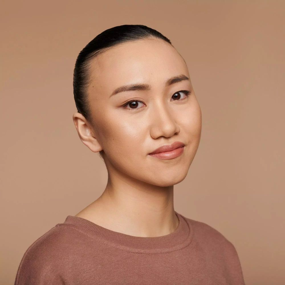 Femme avec peau lisse et fond de teint. Cheveux bruns attachés. Look naturel.