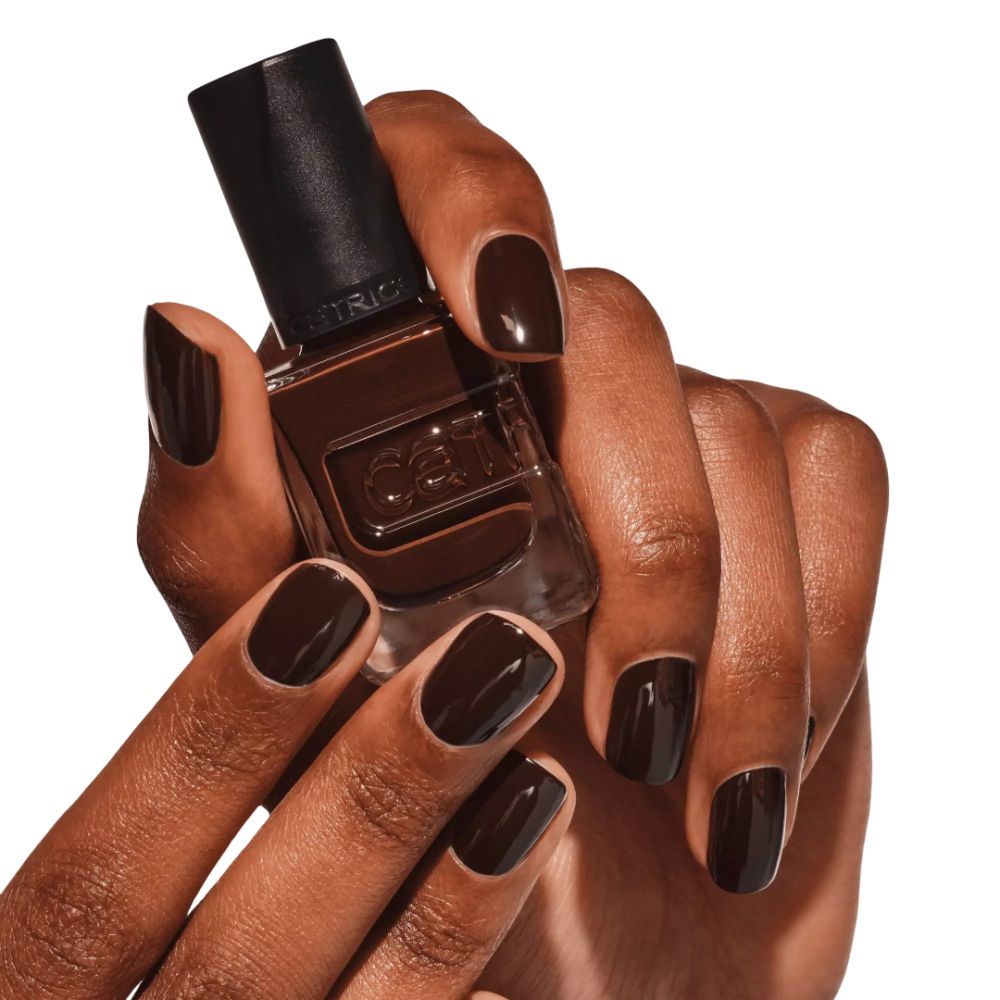 Mains avec ongles vernis en marron tenant un flacon de vernis. Marque Catrice visible.
