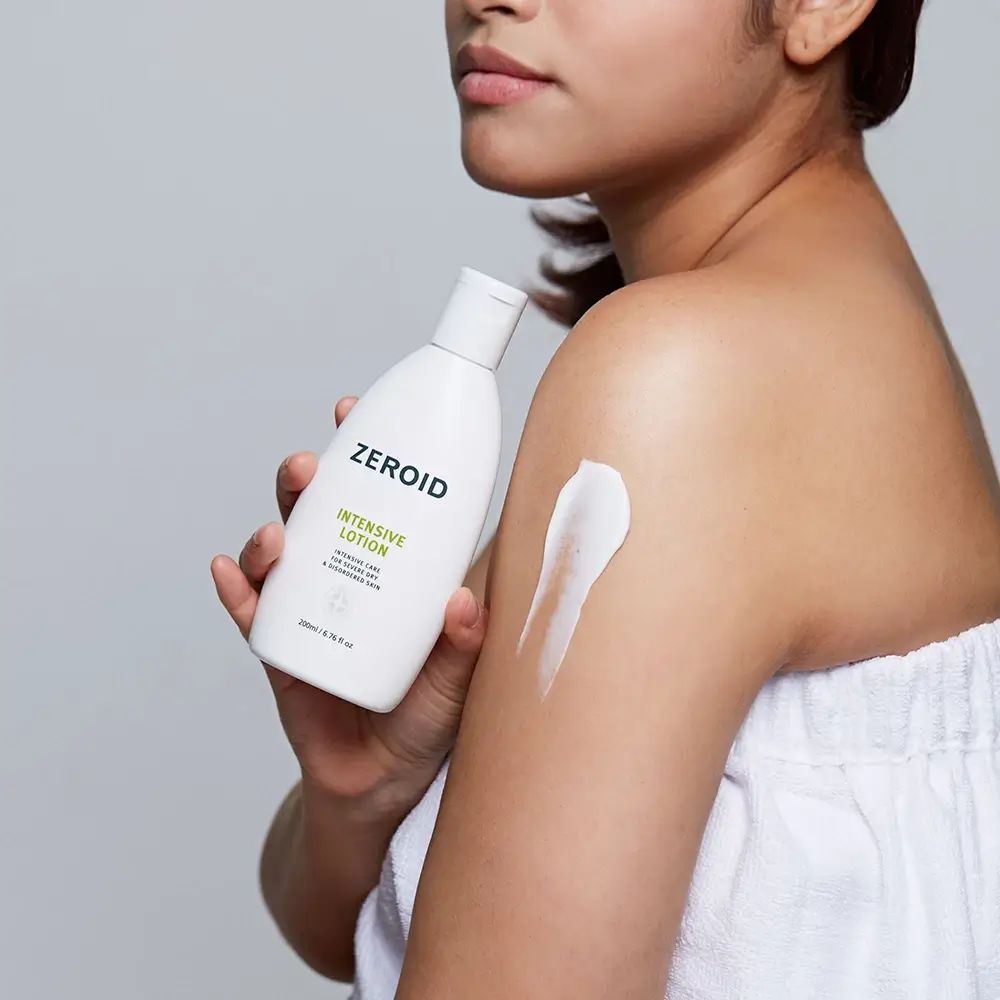 Personne tenant un flacon de ZEROID Intensive Lotion. Crème appliquée sur le bras. Serviette blanche.