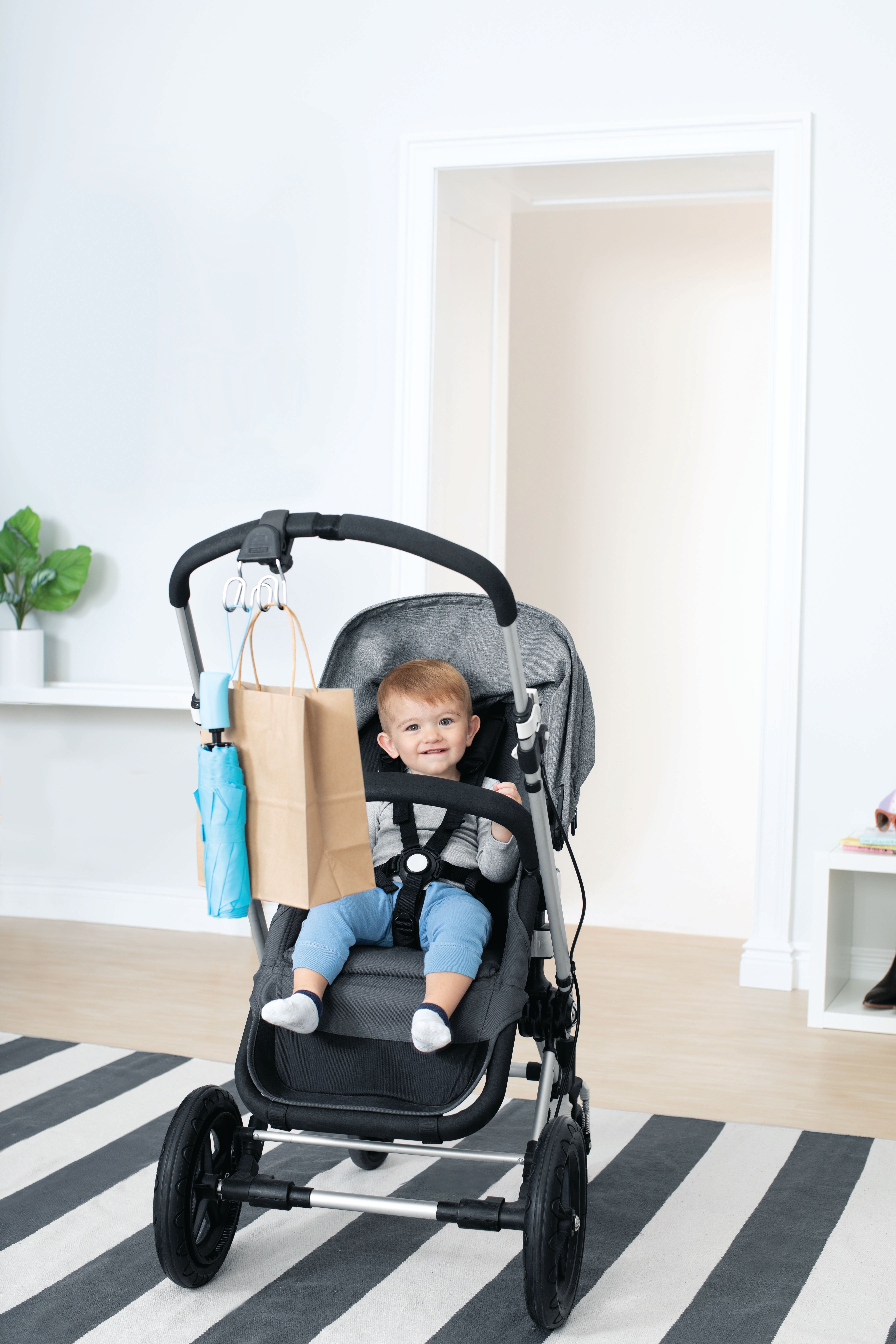 Baby in kinderwagen met haken. Boodschappentas en paraplu.