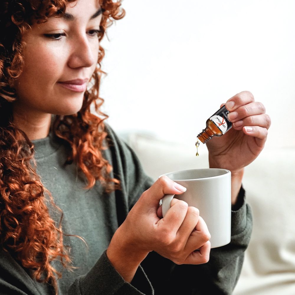 Vrouw giet druppels uit een bruine fles in een witte beker. De fles heeft een etiket.