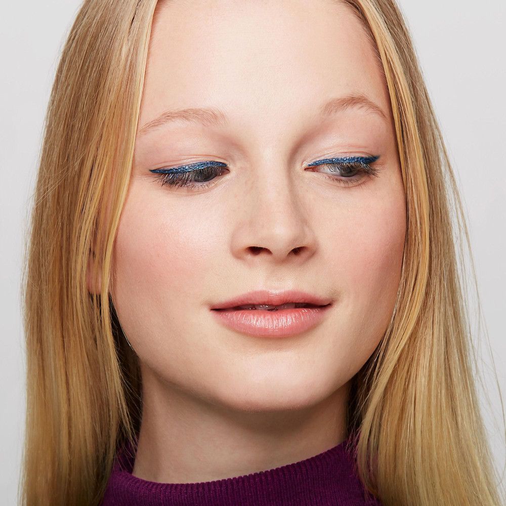 Portrait d'une femme avec un eye-liner bleu. Cheveux blonds, regard vers le bas.